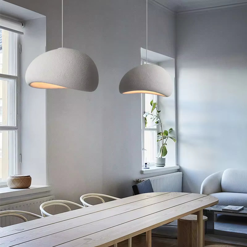 Deux suspensions blanches aux formes organiques et à la texture minérale éclairent une table en bois dans un intérieur scandinave.