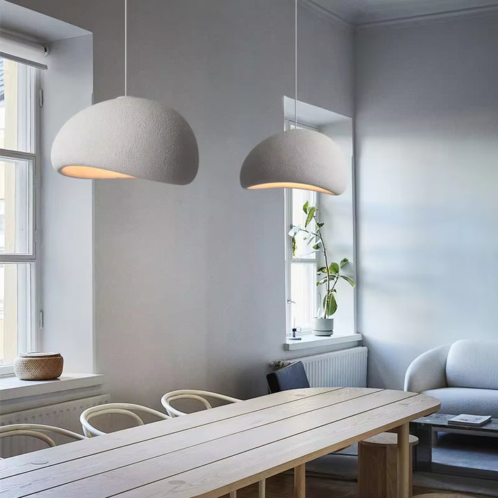 Deux suspensions blanches aux formes organiques et à la texture minérale éclairent une table en bois dans un intérieur scandinave.