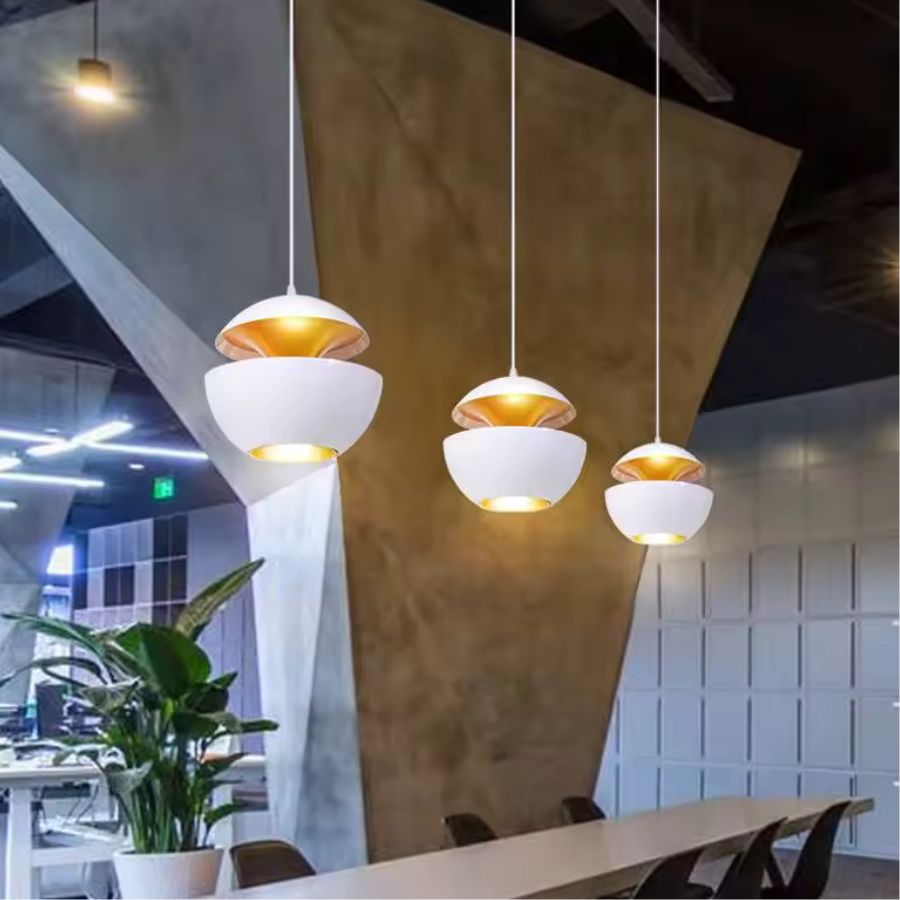 Trois suspensions blanches à double coque métallique et intérieur doré dans un espace au style contemporain