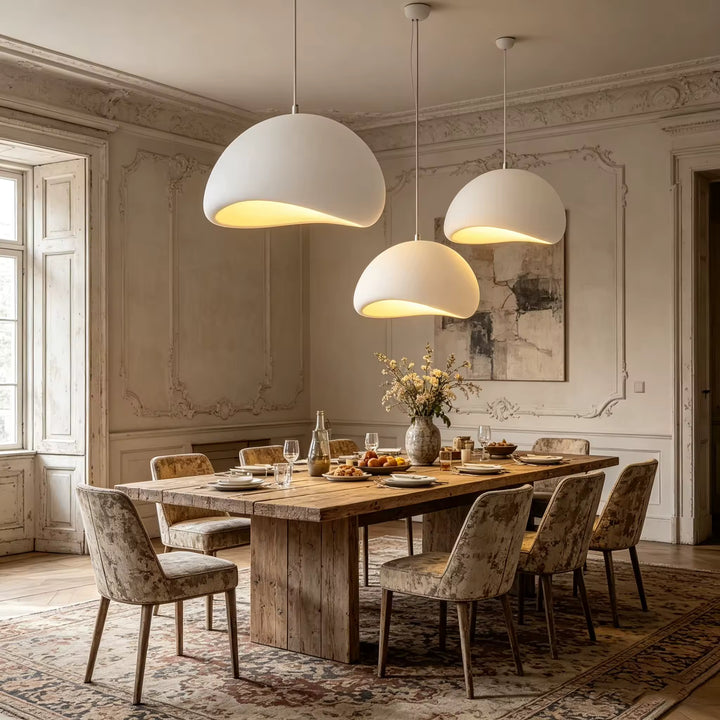 Dans une salle à manger campagne chic aux moulures anciennes, trois suspensions blanches à dômes organiques diffusent une lumière douce.