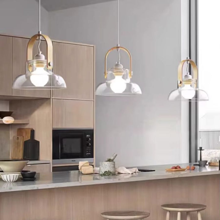 Trois suspensions en bois clair et verre soufflé transparent habillent un îlot de cuisine lumineux au style moderne et naturel
