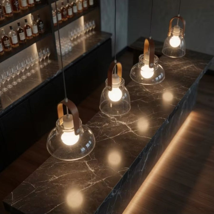 Vue en plongée sur quatre suspensions en bois et verre soufflé au-dessus d’un comptoir en marbre sombre et raffiné