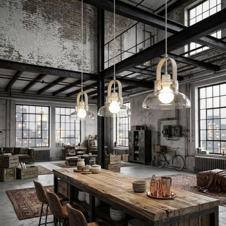 Trois suspensions en bois clair et verre soufflé surplombent une grande table dans un loft industriel au charme brut
