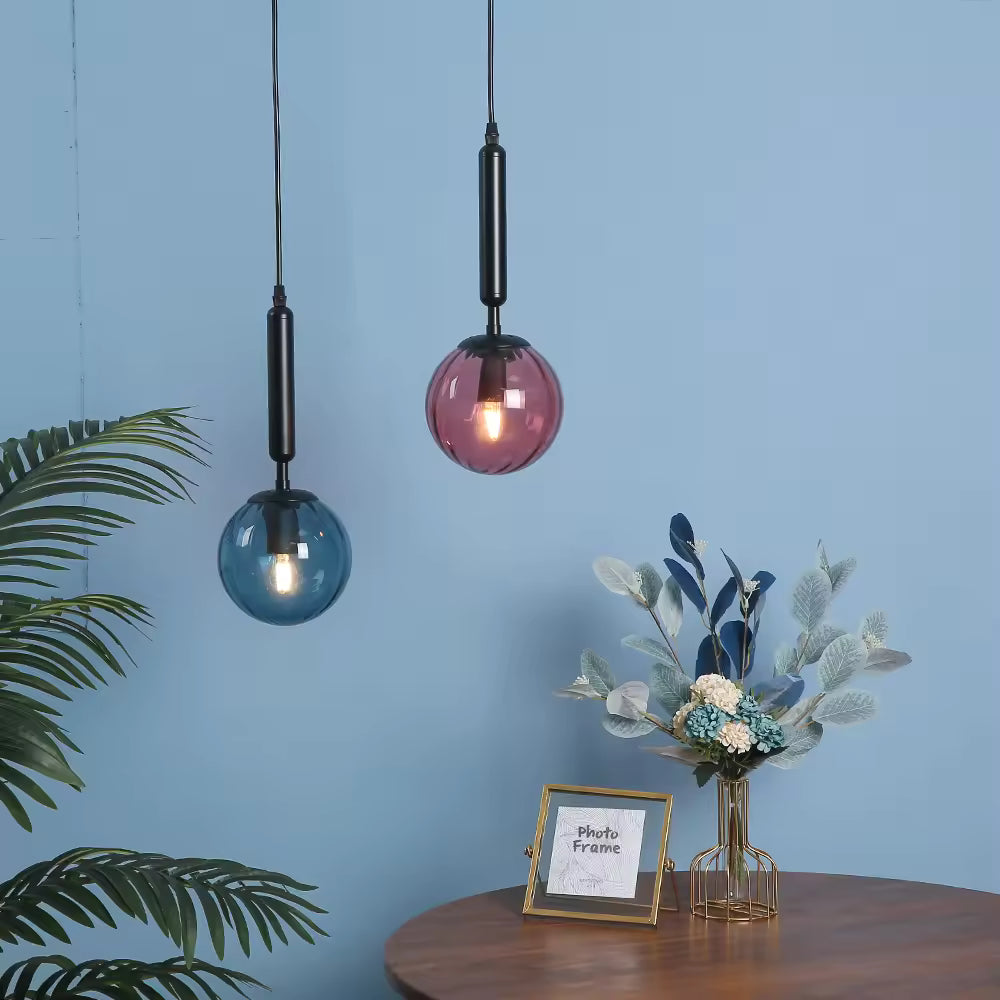 Duo de suspensions boule en verre bleu et rose, tiges noires élancées dans un intérieur moderne aux accents décoratifs