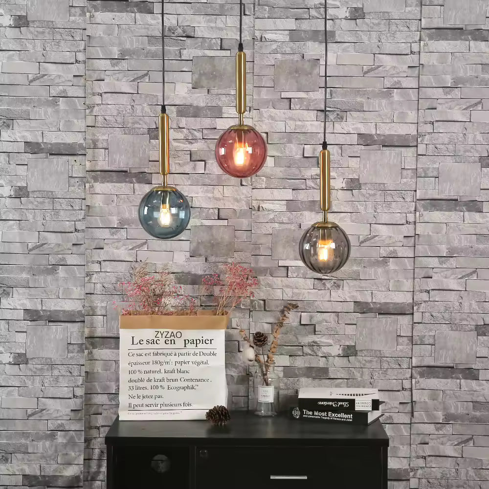 Trois suspensions boule en verre coloré avec tiges dorées, dans une ambiance moderne aux accents rétro chic