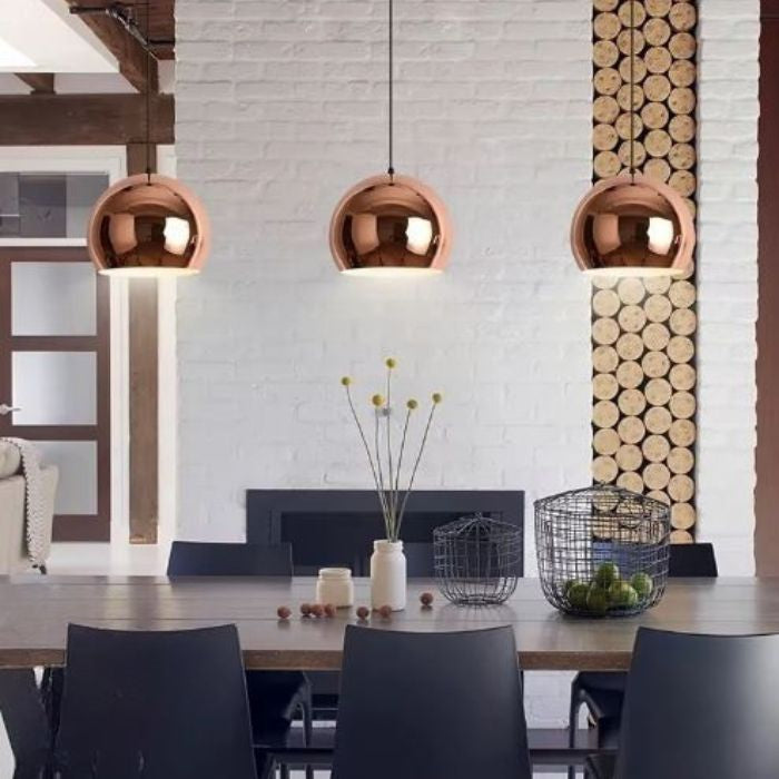 Trois suspensions boules cuivre rose dans une salle à manger, luminaires scandinaves chic au design contemporain chaleureux.