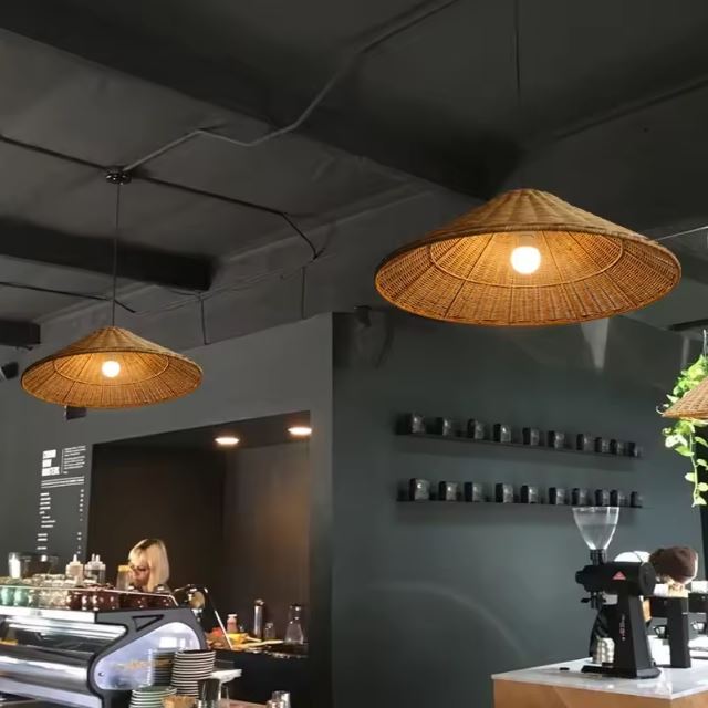 Suspensions chapeau en rotin naturel éclairant un café moderne au design sombre et épuré.