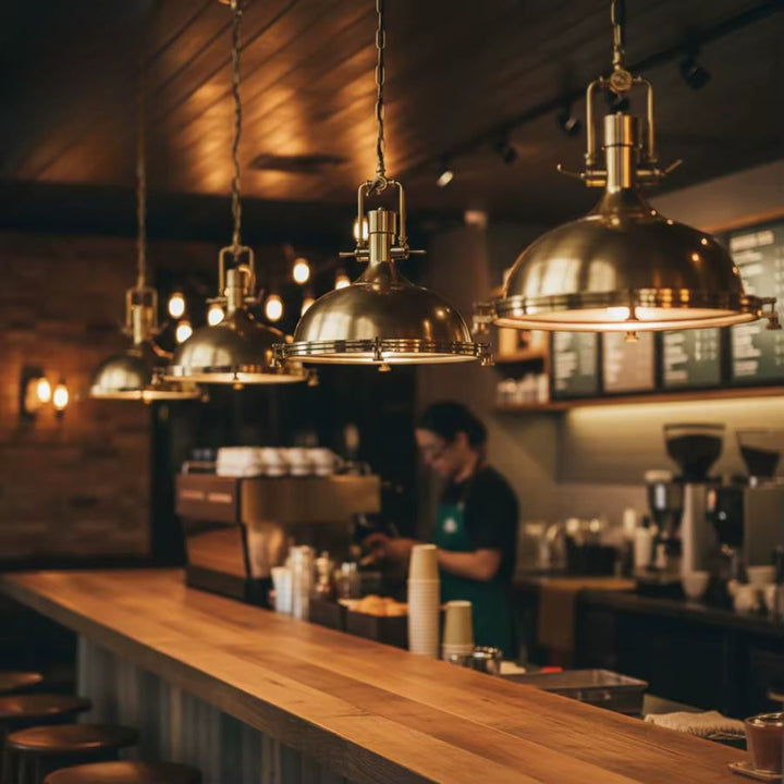 Plusieurs suspensions cloche en métal éclairent un comptoir de café dans une ambiance industrielle vintage