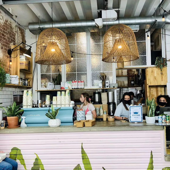 Deux suspensions en rotin tressé à double abat-jour éclairent le comptoir d'un café au style industriel et bohème.