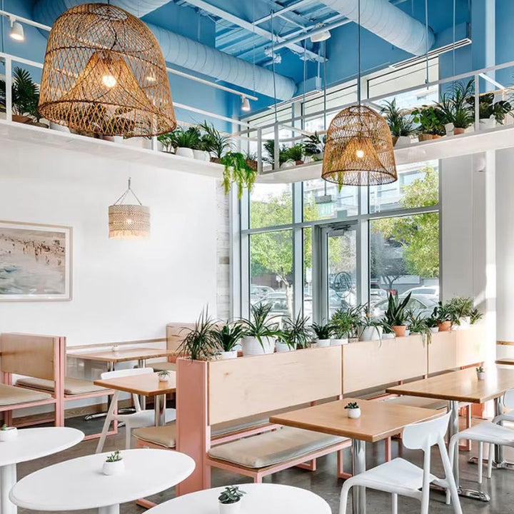 Deux grandes suspensions cloche en rotin ajouré habillent un café lumineux au décor végétal et à l'esprit bohème naturel.