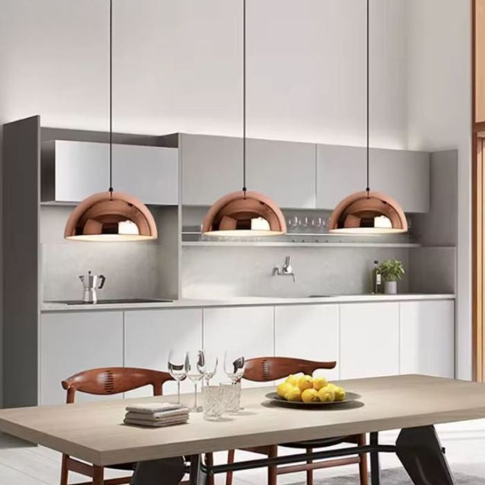 Trois suspensions cuivre rose au-dessus d’une table, luminaires contemporains au style design italien et rétro chic.