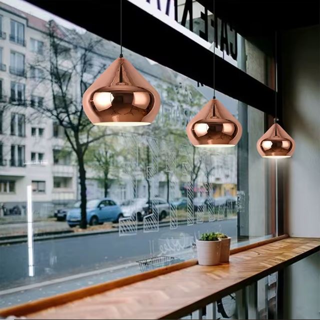 Suspensions en cuivre rose dans un café avec vue sur la vitrine, ajoutant élégance et lumière chaleureuse.