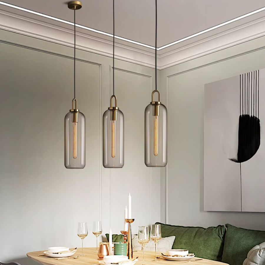 Trois suspensions cylindriques en verre transparent à anse dorée dans une salle à manger élégante et contemporaine