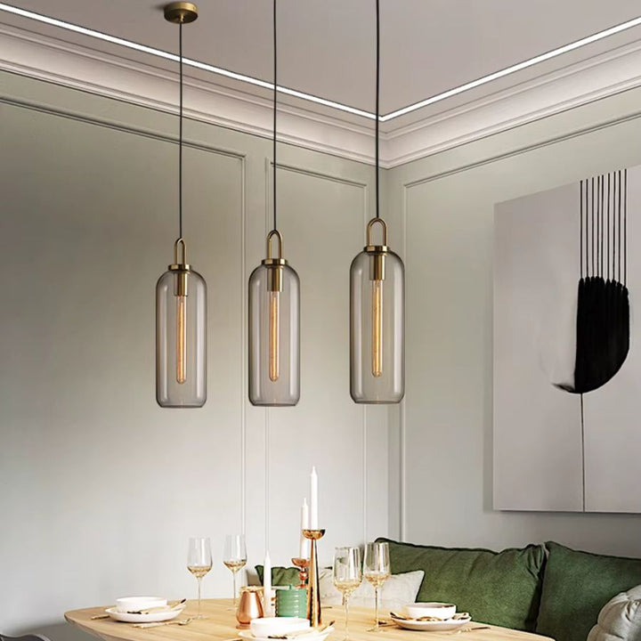 Trois suspensions cylindriques en verre transparent à anse dorée dans une salle à manger élégante et contemporaine