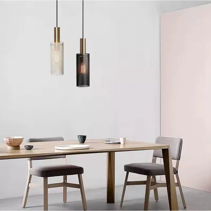 Au-dessus d’une table à manger, deux suspensions ajourées noire et blanche mêlent métal doré et design contemporain