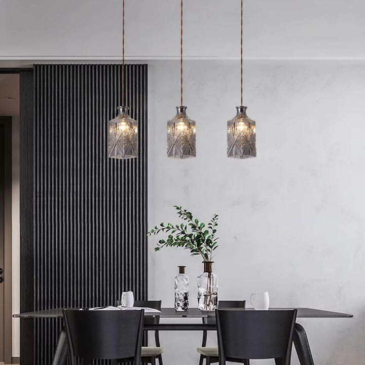 Trois suspensions flacon en verre taillé au-dessus d’une table, dans une salle à manger contemporaine et élégante