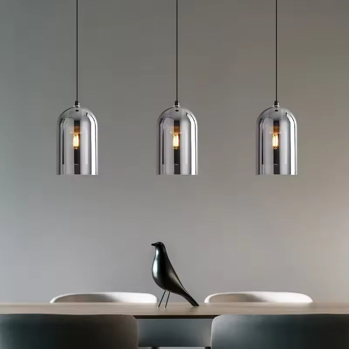 Trois suspensions en verre fumé au design industriel chic, alignées au-dessus d'une table de salle à manger.