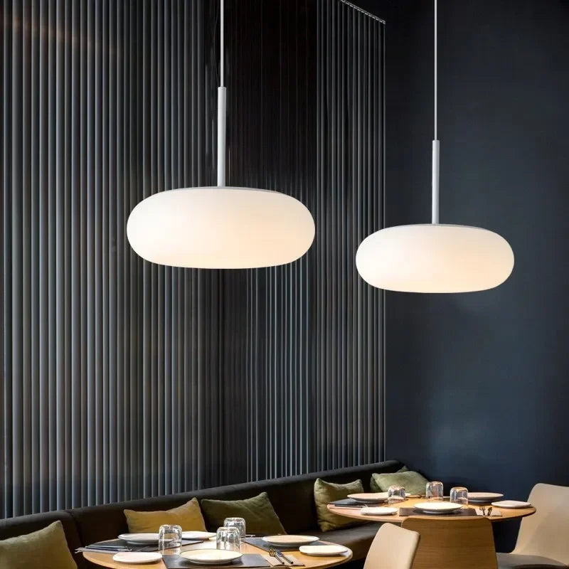 Deux luminaires galet flottant en verre opalin suspendus dans une ambiance feutrée.