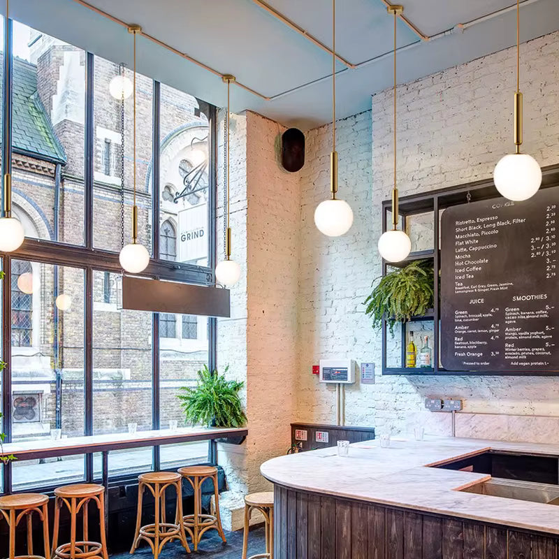 Série de suspensions globe blanches à longues tiges dorées, dans un café lumineux au style industriel chic et contemporain