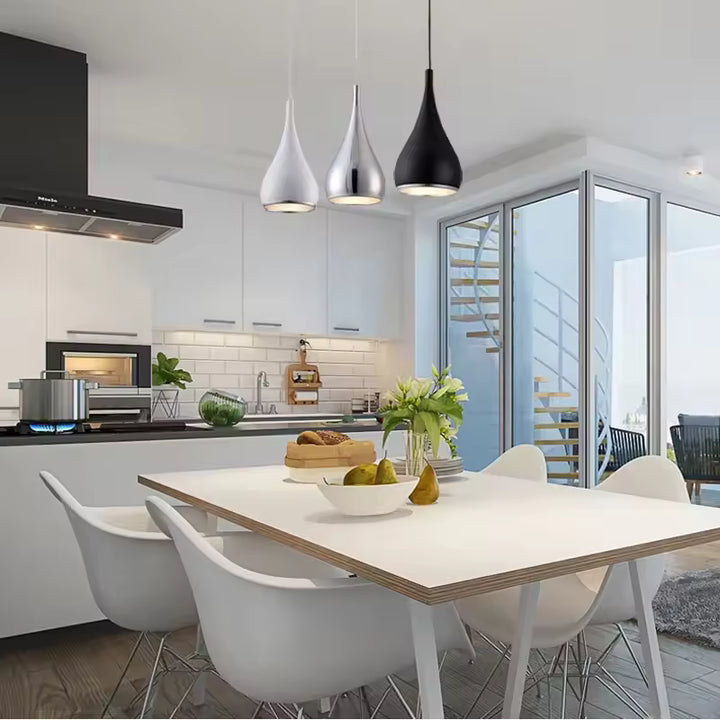 Dans une cuisine moderne, trois suspensions goutte en métal blanc, chromé et noir éclairent la table à manger