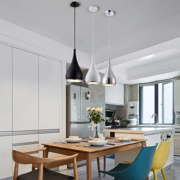 Alignées au-dessus de la table, trois suspensions goutte en métal noir, blanc et chromé apportent un style moderne