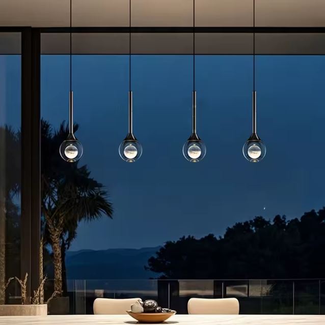 Suspensions goutte en verre transparent et métal noir alignées devant baie vitrée, éclairage design contemporain et élégant.