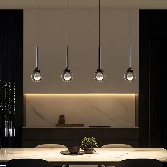 Alignement de suspensions goutte en verre type cristal et métal noir au-dessus d’une table, éclairage design contemporain et luxueux.