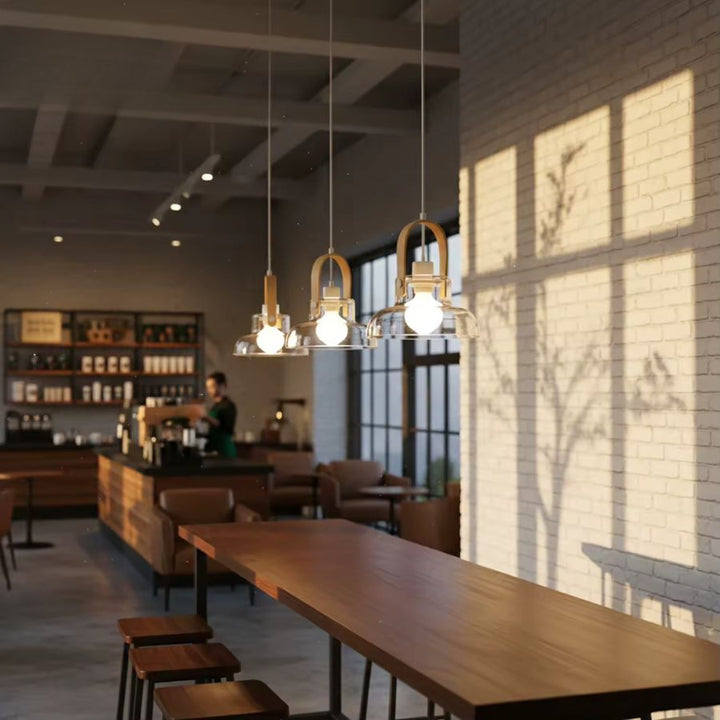 Dans un café au décor industriel, trois suspensions en bois et verre soufflé éclairent une grande table en bois