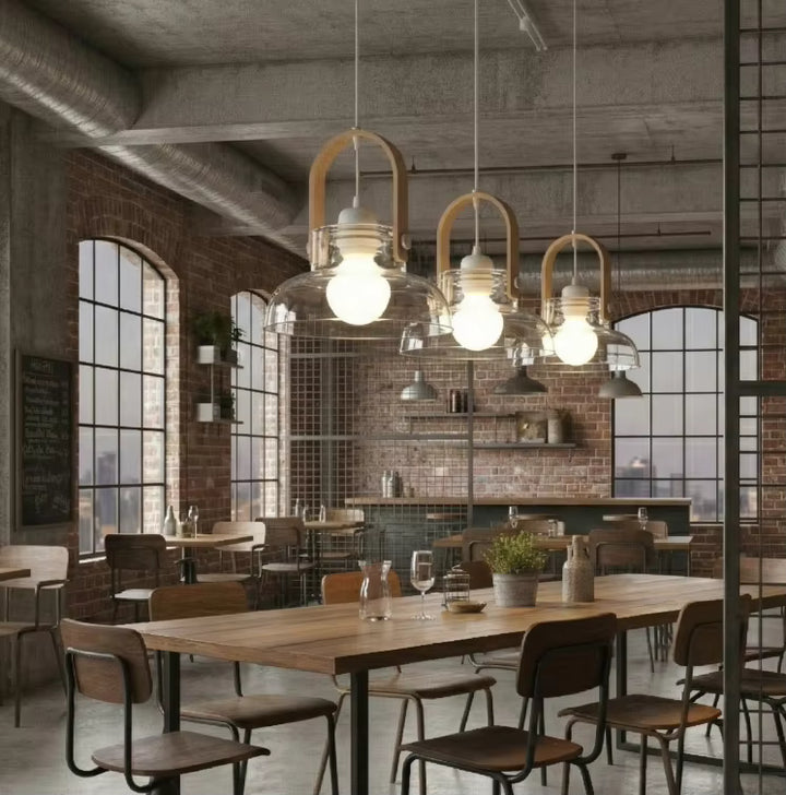 Trois suspensions lanterne en bois clair et verre soufflé illuminent un restaurant au décor industriel chaleureux