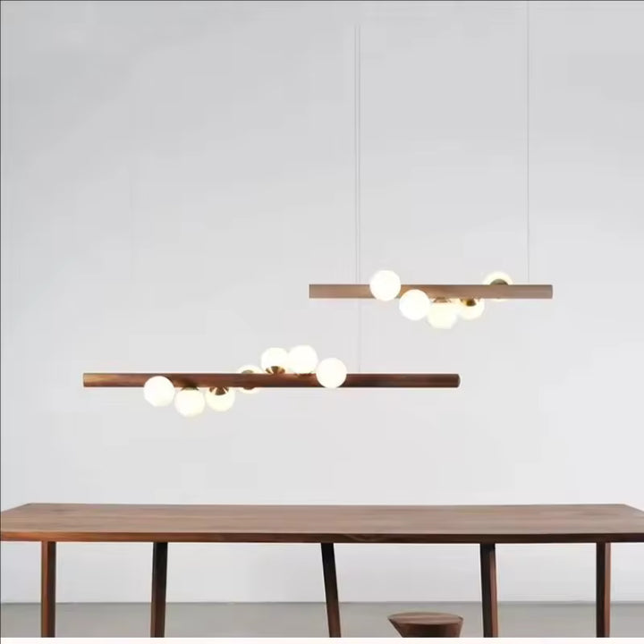 Deux suspensions linéaires en bois à globes lumineux, dans une composition minimaliste aux influences scandinaves et japandi.