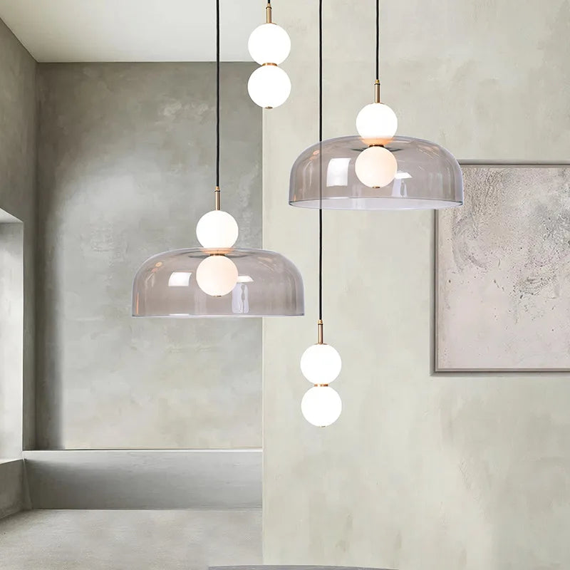 Composition élégante de plusieurs suspensions design en verre transparent légèrement fumé avec des sphères lumineuses blanches.
