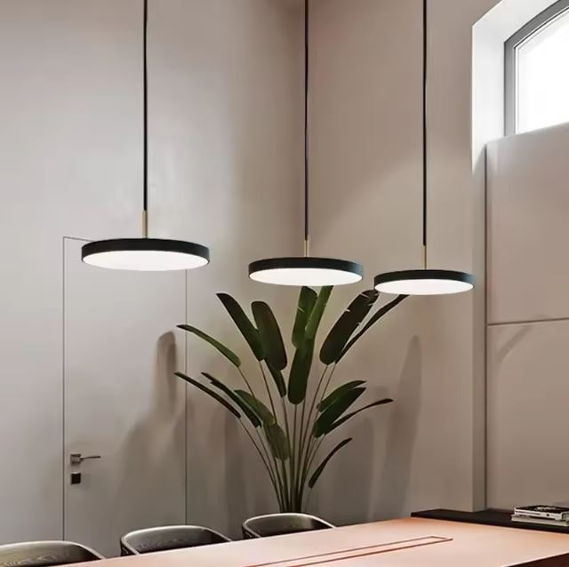 Trois suspensions plates noires suspendues au-dessus d'une table moderne dans une salle à manger lumineuse et élégante avec une plante décorative.