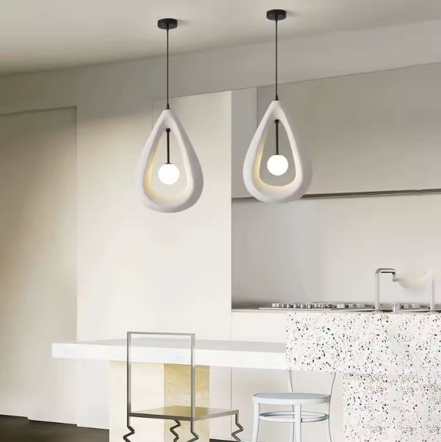 Deux suspensions en plâtre au design organique éclairant une cuisine moderne avec un îlot en terrazzo et des chaises minimalistes.