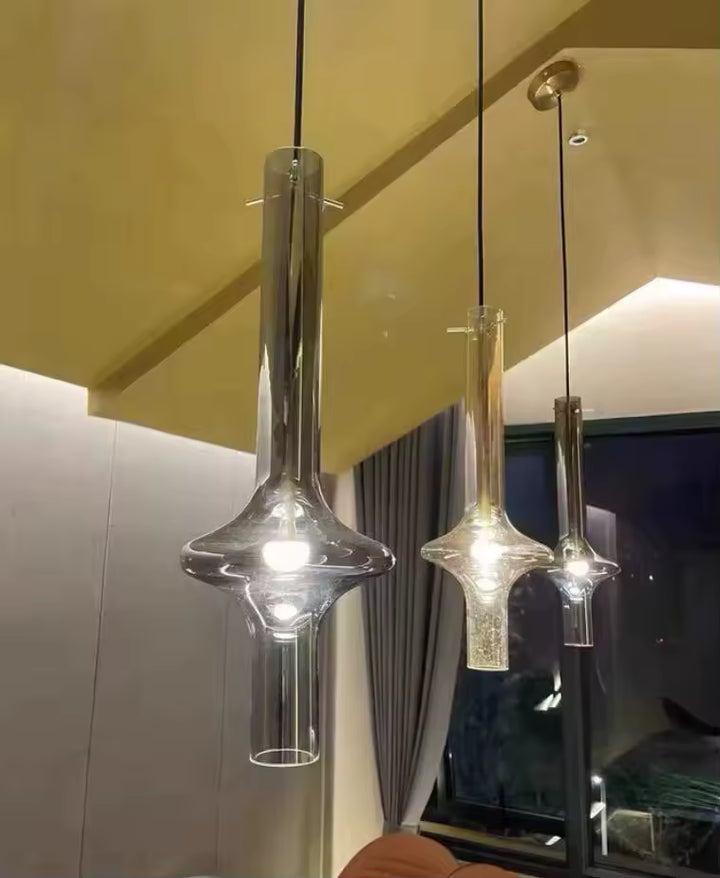 Trois suspensions totem en verre transparent, fumé et cognac aux formes élancées, dans un intérieur moderne et architectural