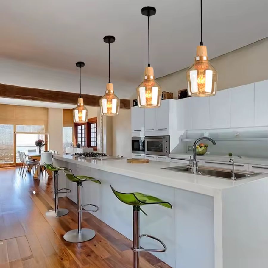 Au-dessus d’un îlot de cuisine, plusieurs luminaires en verre ambré et bois créent une ambiance chaleureuse et moderne