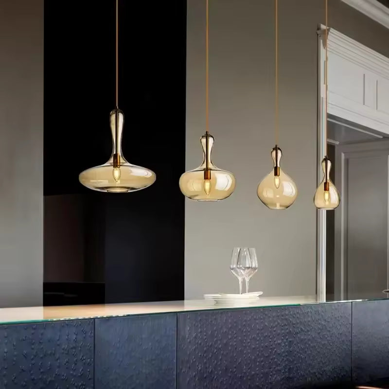 Alignement de quatre suspensions en verre ambré aux formes sculpturales, au-dessus d'un îlot de cuisine contemporain.