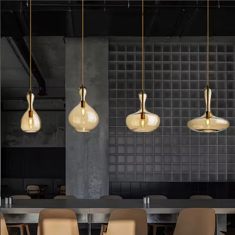 Quatre suspensions en verre ambré aux courbes sculpturales, alignées dans un espace de restauration au style industriel.