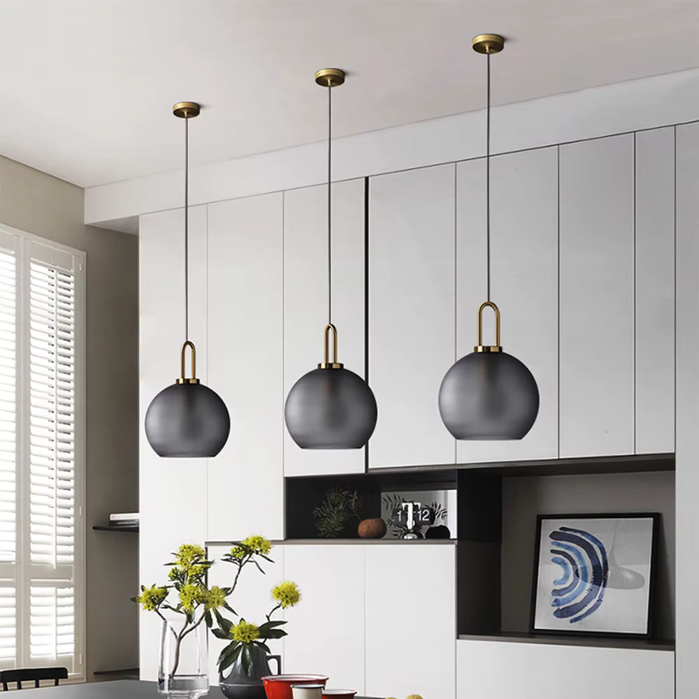 Trois suspensions globe en verre fumé à anse dorée dans une salle à manger moderne au style élégant