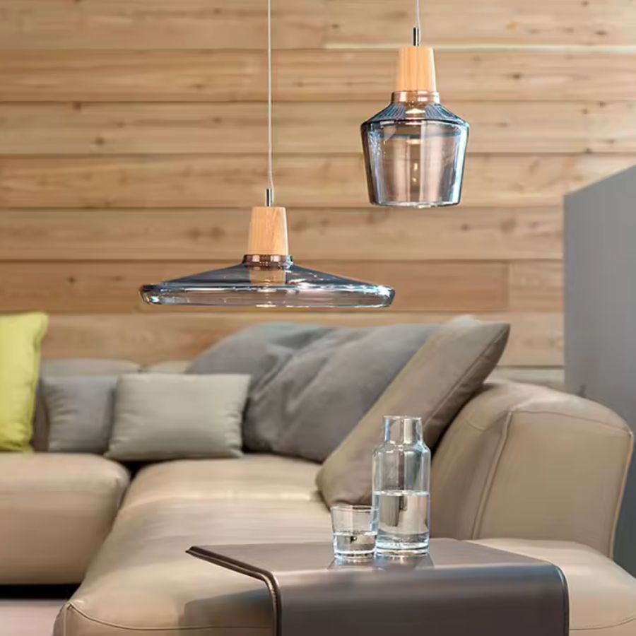 Deux modèles en verre fumé et bois habillent un salon moderne avec une esthétique légère et sculpturale