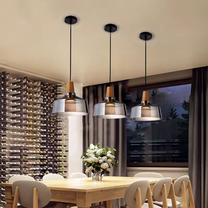 Trois suspensions en verre fumé et bois éclairent une grande table de salle à manger au style contemporain