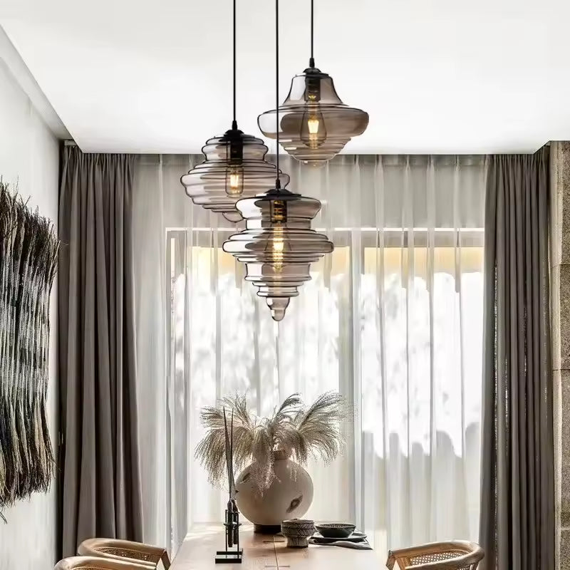 En cascade au-dessus d'une table en bois, trois suspensions en verre fumé aux formes sculpturales habillent un intérieur raffiné.