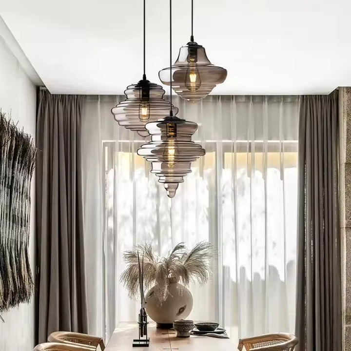 En cascade au-dessus d'une table en bois, trois suspensions en verre fumé aux formes sculpturales habillent un intérieur raffiné.
