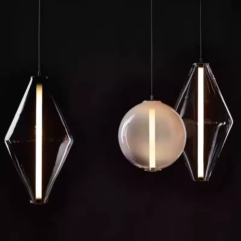 Trois suspensions en verre de formes losange et sphérique au design graphique, chacune structurée par une ligne lumineuse verticale