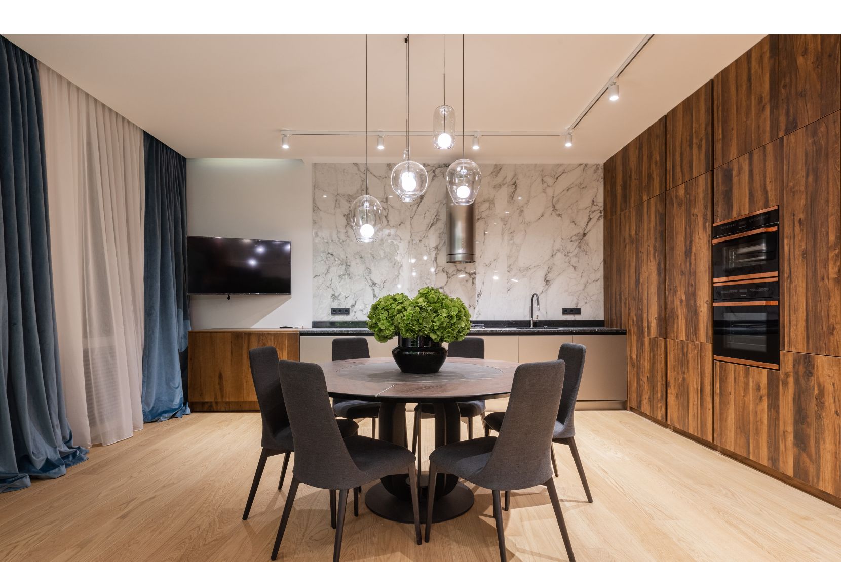 Suspensions en verre design au-dessus d'une table ronde dans une cuisine moderne avec mur en marbre et bois.