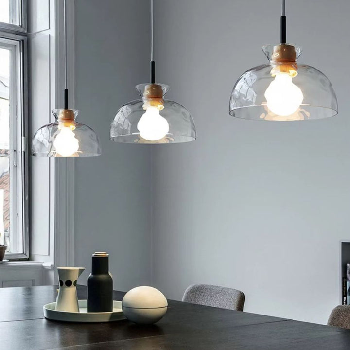 Trois suspensions en verre ondulé et bois alignées au-dessus d’une table, dans un intérieur scandinave épuré