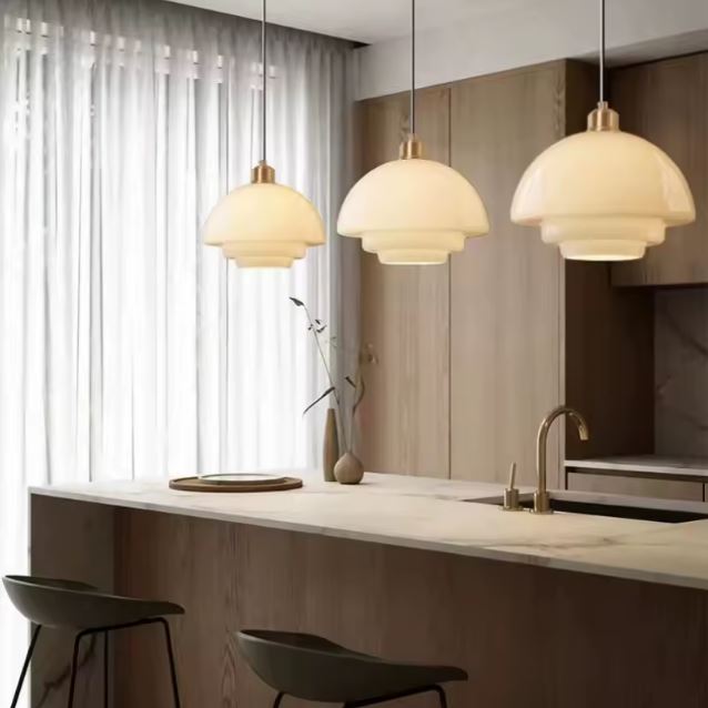 Trois suspensions en verre opaline illuminant un bar de cuisine moderne avec un style minimaliste et épuré.