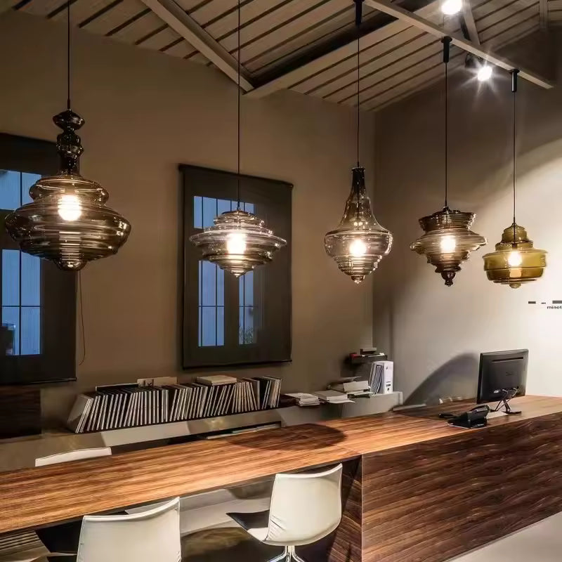 Cinq suspensions sculpturales en verre fumé et ambré, aux reliefs étagés, éclairent un comptoir en bois moderne.