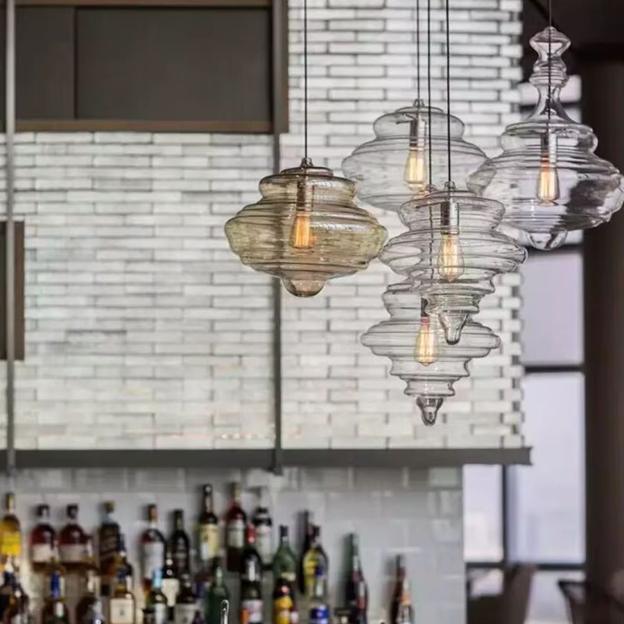 Composition de suspensions en verre transparent et ambré aux reliefs sculpturaux, au-dessus d'un bar de style industriel.