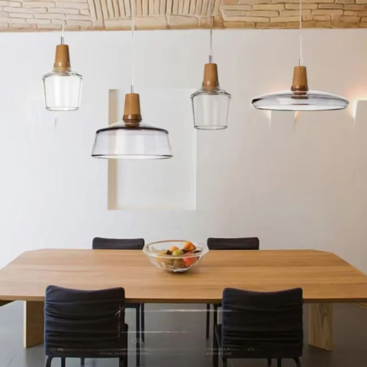 Au-dessus d’une table en bois, plusieurs suspensions en verre transparent apportent un esprit naturel et épuré