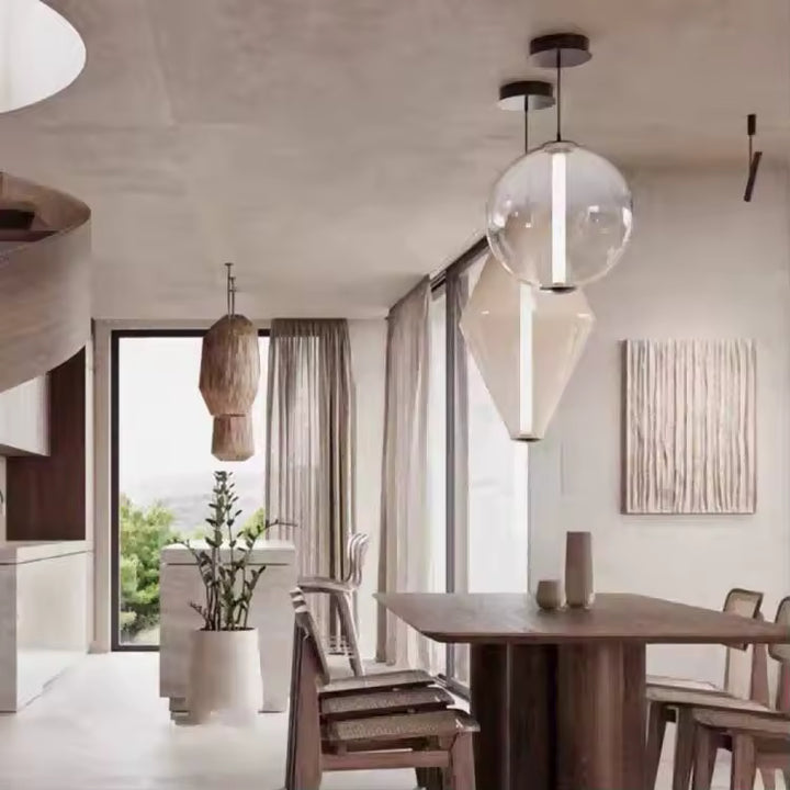 Duo de luminaires suspendus en verre transparent, entre forme sphérique et silhouette géométrique, dans une salle à manger moderne